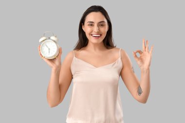 Alarmlı saati olan pijamalı genç bir kadın açık arkaplanda iyi görünüyor.