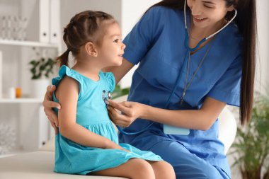 Steteskoplu kadın çocuk doktoru. Klinikteki küçük tatlı kızı dinliyor.