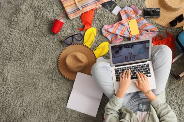 Yeşil halıda plaj aksesuarları olan dizüstü bilgisayar kullanan kadın seyahat blogcusu, üst görünüm