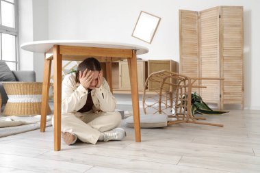 Deprem sırasında oturma odasında masanın altında saklanan genç bir kadın.