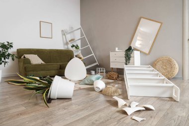 Ters dönmüş masa, raf üniteleri ve depremden sonra bitkilerle dolu dağınık bir oturma odası.