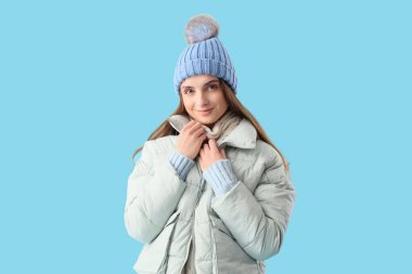 Mavi arka planda şık, sıcak giysiler içinde güzel genç bir kadın.