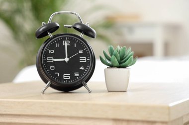 Siyah çalar saat. Yatak odasındaki masada bitki var. Yakın plan.