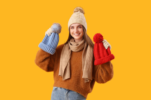 Красивая молодая женщина в теплой одежде в стильных шляпах на желтом фоне