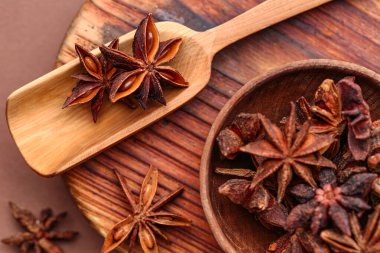 Ahşap tahta tahtada bir kase aromatik yıldız anason ve renkli arka planda kepçe, yakın plan.