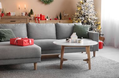 Noel için dekore edilmiş oturma odasının içinde masa üzerinde kanepe ve ev şeklinde mum tutacakları var.