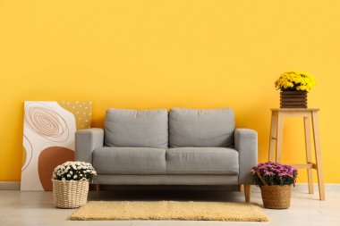 Oturma odasında kanepe, masa ve kasımpatı çiçekleri var.