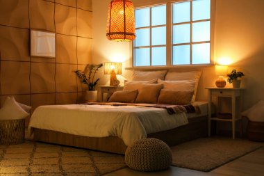 Geceleri yatak odasının içinde masalar, bitkiler ve parlayan lambalar var.