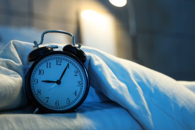 Gecenin karanlığında yatak odasında battaniyeli çalar saat, yakın plan.