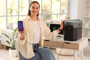 Genç bir kadın evdeki portatif elektrik santraliyle cep telefonunu şarj ediyor.