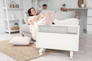 Çoraplı genç bir kadın ayaklarını elektrikli konteyner ısıtıcısında ısıtıyor.