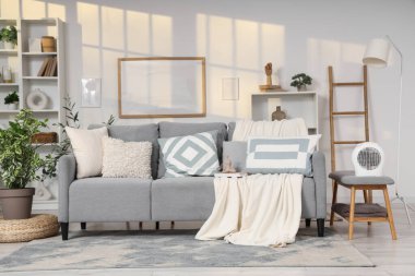 Oturma odasının içinde kanepe ve elektrikli vantilatör var.