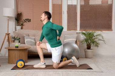 Sportif genç adam evdeki spor minderinde sırt ağrısı çekiyor.