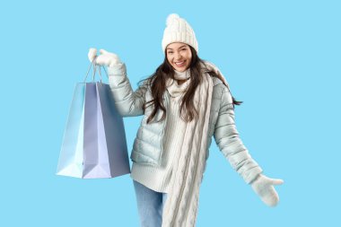 Mavi arka planda alışveriş torbaları olan kışlık elbiseli genç bir kadın.