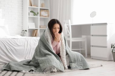 Yatak odasında sıcak ekose kumaşlı donmuş genç bir kadın oturuyor.