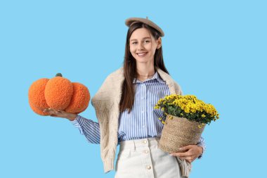 Kasımpatı çiçekleri ve mavi arka planda balkabağı yastığı olan şık genç bir kadın.