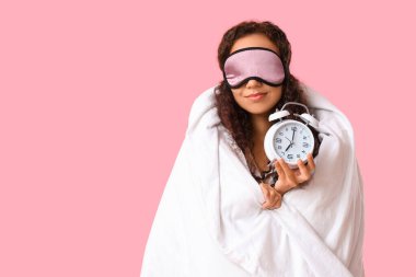 Pembe arka planda battaniyesi ve çalar saati olan güzel, mutlu bir Afro-Amerikalı kadın.