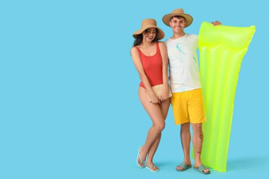 Mavi arka planda şişme yatağı olan mutlu genç çift.