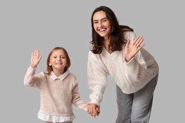 Anne ve küçük kızı gri arka planda el sallıyorlar.