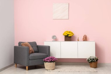 Oturma odasının içinde koltuk, tuvalet ve kasımpatı çiçekleri var.