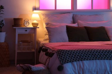 Geceleri karanlık yatak odasındaki masada parlayan lambalı çalar saat.