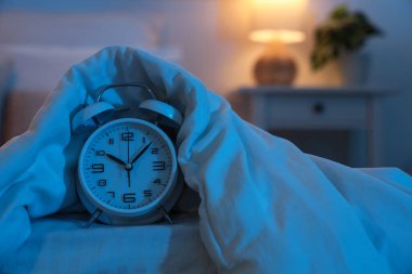 Gecenin karanlığında yatak odasında battaniyeli çalar saat, yakın plan.