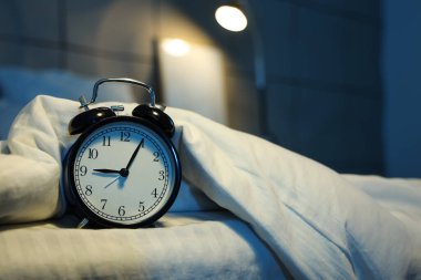 Gecenin karanlığında yatak odasında battaniyeli çalar saat, yakın plan.