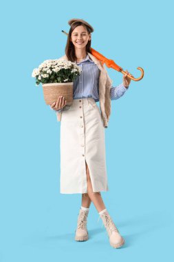 Kasımpatı çiçekleri ve mavi arka planda şemsiyesi olan şık genç bir kadın.