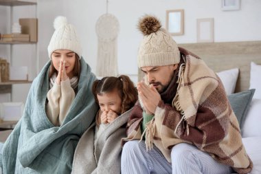 Ekoseli ve ısıtma eksikliği olan donmuş bir aile yatak odasında oturuyor.