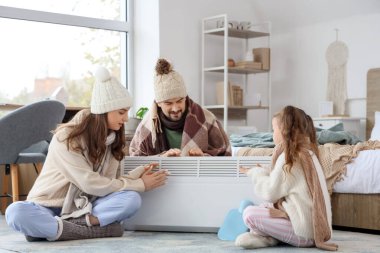 Yatak odasındaki elektrikli konteyner ısıtıcısının yanında donmuş aile ısınması.