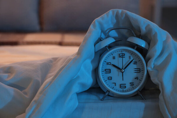 Retro alarm clock with blanket on bed in dark bedroom at night, closeup