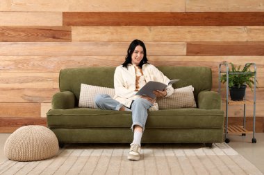 Evdeki yeşil koltukta dergi okuyan güzel bir kadın.