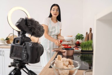 Genç bir kadın mutfakta yemek pişirirken kaseye çorba dolduruyor.