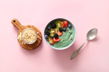 Bir kase lezzetli spirulina smoothie ve pembe arka planda böğürtlen.