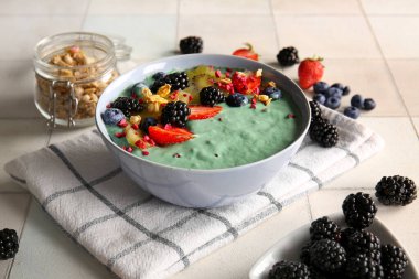 Bir kase lezzetli spirulina smoothie ve fayans zemininde böğürtlen, yakın plan.