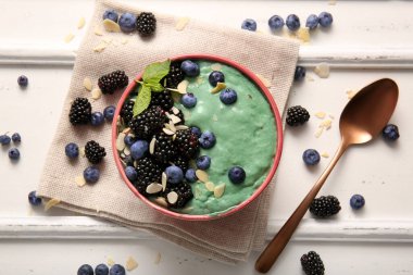 Peçete, lezzetli spirulina smoothie ve beyaz arka planda böğürtlenli kase.