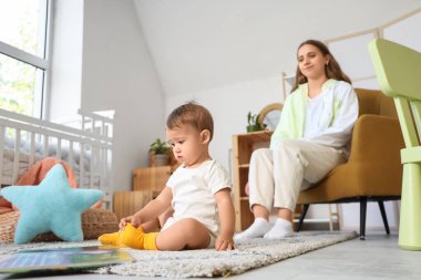 Kitabı halıya oturmuş, annesi evde olan tatlı bir kız.