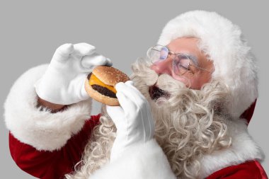 Noel Baba gri arka planda lezzetli bir burger yiyor.