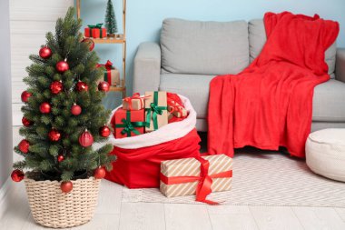 Konforlu kanepe, Noel ağacı ve içinde oturma odasının içi hediyelerle dolu Noel Baba çantası.