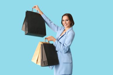 Mavi arka planda alışveriş torbaları olan güzel genç bir kadın. Kara Cuma konsepti