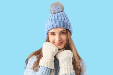 Mavi arka planda şık, sıcak giysiler içinde güzel genç bir kadın.