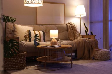 Oturma odasında rahat bir kanepe, sehpa ve akşam lambaları var.