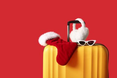 Güneş gözlüklü bavul ve kırmızı arka planda Noel süsü. Yakın çekim.