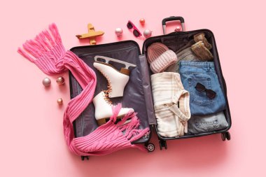 İçinde kışlık giysiler ve pembe arka planda Noel dekoru olan bavulu aç. Üst görünüm