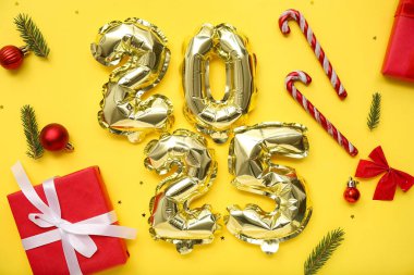Noel topları, şeker kamışları, hediye kutuları ve sarı arka planda köknar dalları olan folyo balonlardan yapılmış 2025 model.