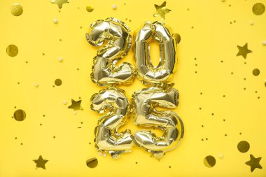 Sarı arka planda folyo balonlardan ve konfetiden yapılmış 2025 model. Noel kutlaması