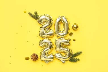 Çam kozalaklı folyo balonlardan ve sarı arka planda Noel ağacı dallarından oluşan 2025 numaralı figür.