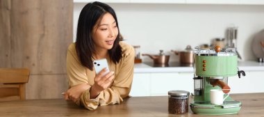 Mutfakta cep telefonu ve kahve makinesi olan Sian kadın.