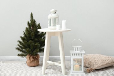 Yanan mumlar ve gri duvarın yanında Noel ağacı olan fenerler.