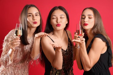 Şampanyalı genç ve güzel kadınlar kırmızı arka planda öpüşüyorlar. Yeni yıl kutlaması